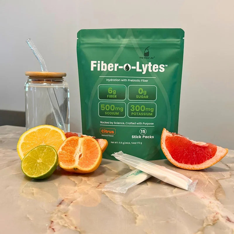 Fiber-O-Lytes citrus electrolyte drink mix with prebiotic fiber, pouch and stick packs beside citrus fruit and a water jar